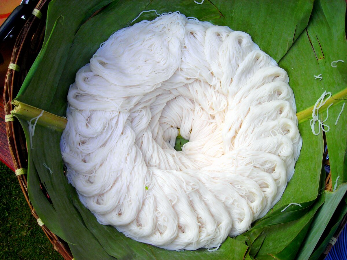 A coil of fresh white rice noodles on a banana leaf, the base of khanom jeen