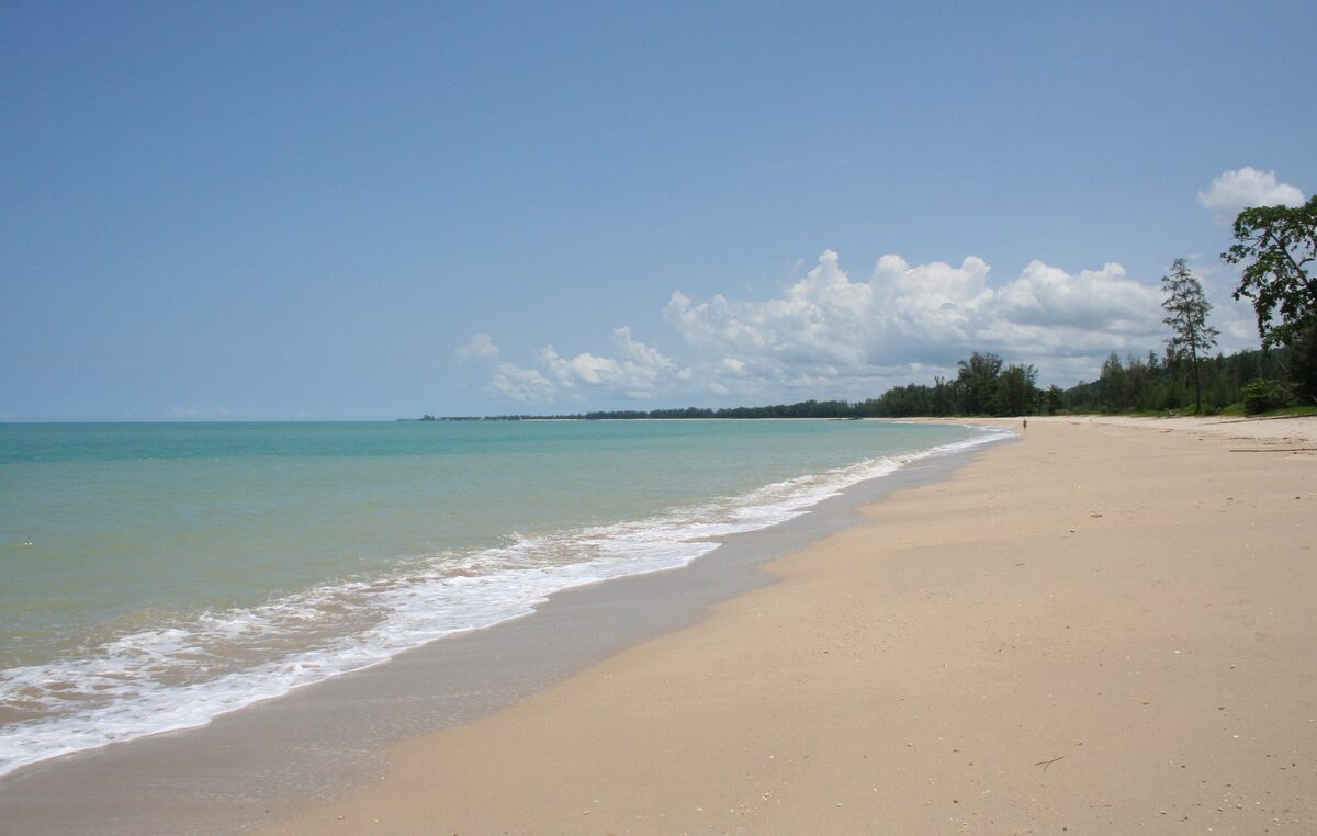 Waves roll across the wide sand of Khao Lak beach, with trees along the shore