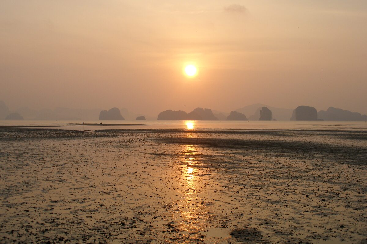 The sun rises in an orange haze over the tidal flats of Koh Yao Noi, with limestone karsts of Phang Nga Bay on the horizon