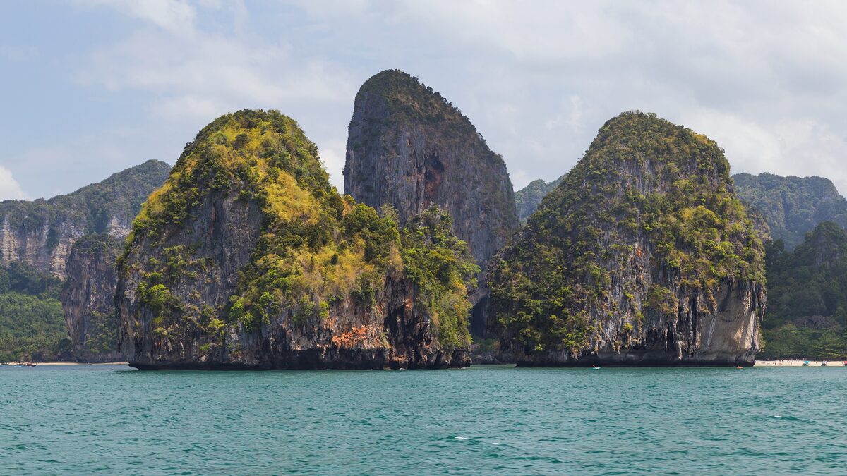 Limestone karsts rise from the green water of the Krabi coast, seen from a boat near Ao Nang