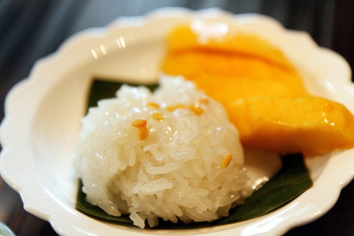A scoop of sticky rice with sesame seeds and slices of ripe mango on a banana leaf in a small scalloped bowl