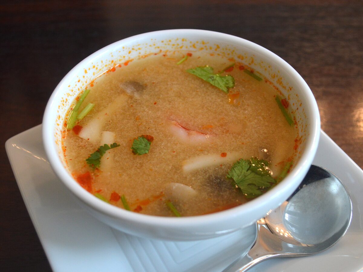 A bowl of red, sour tom yum soup with shrimp, mushrooms and herbs