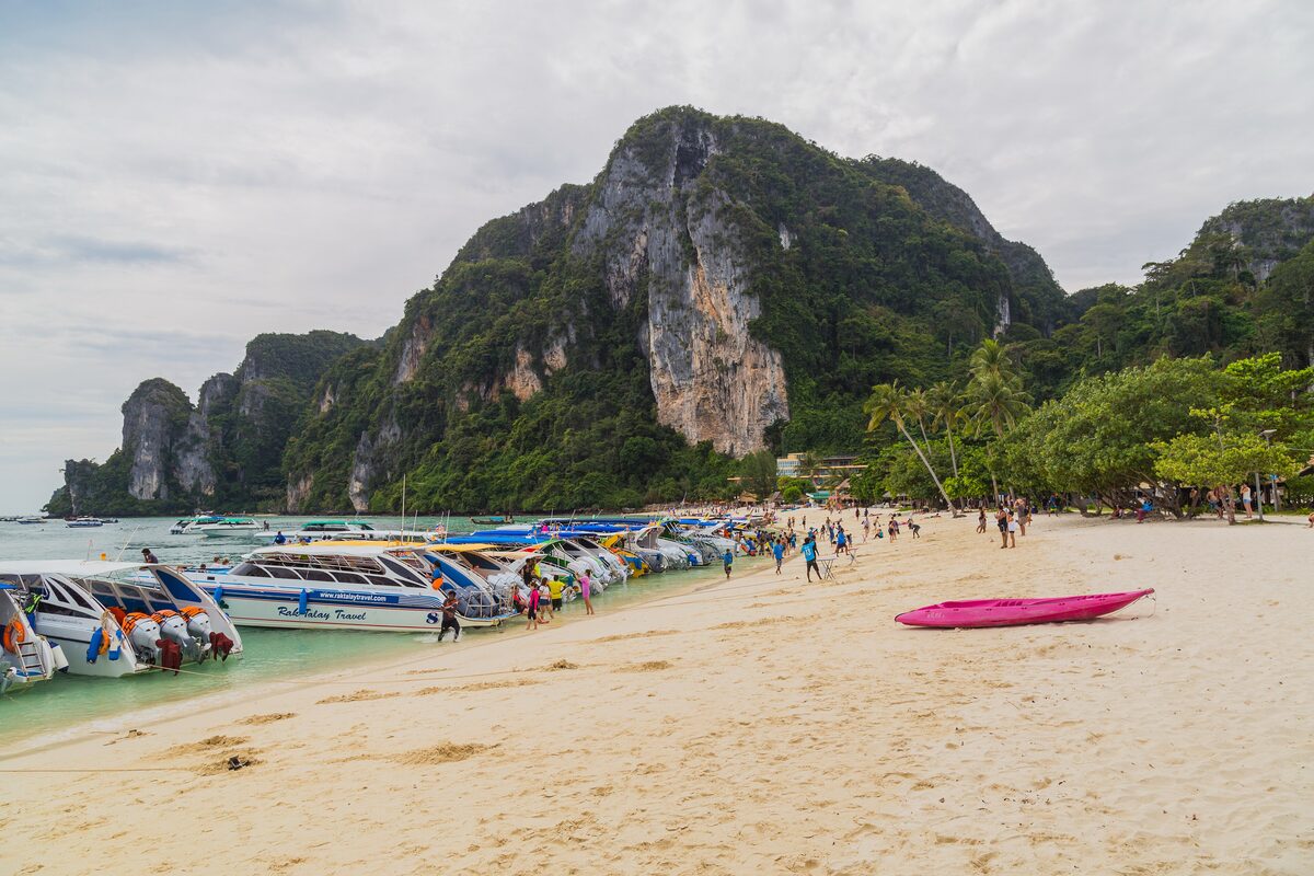 Longtail boats lined up on the sand at Ton Sai beach, with a limestone cliff behind the village