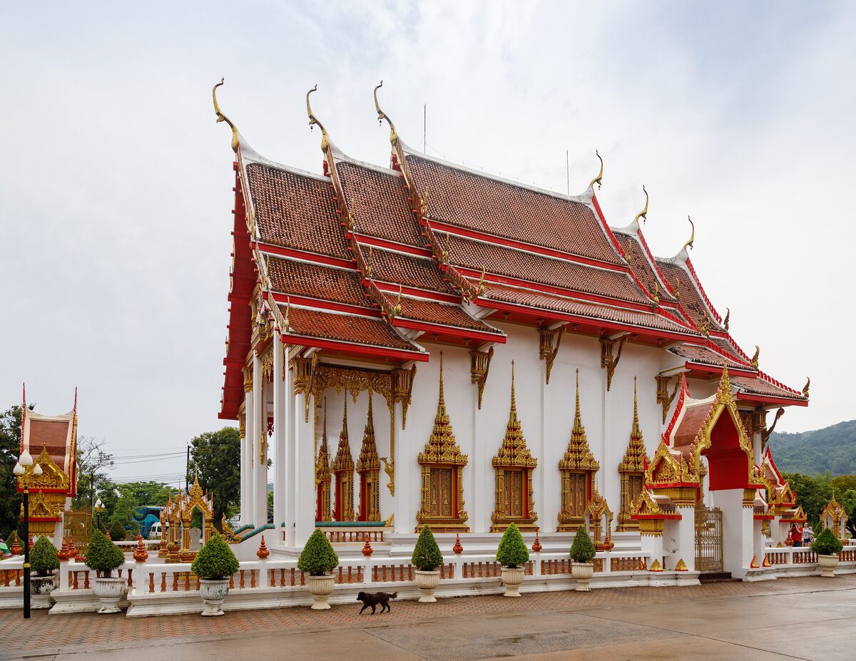 The white ordination hall of Wat Chalong, with red roofs and gold details under a cloudy sky