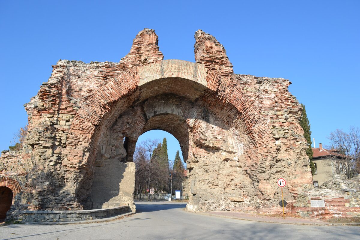 The Kamilite (Camels), the double-humped Roman south gate of Hisarya built of stone and brick, with a road passing through its arch under a clear blue sky.