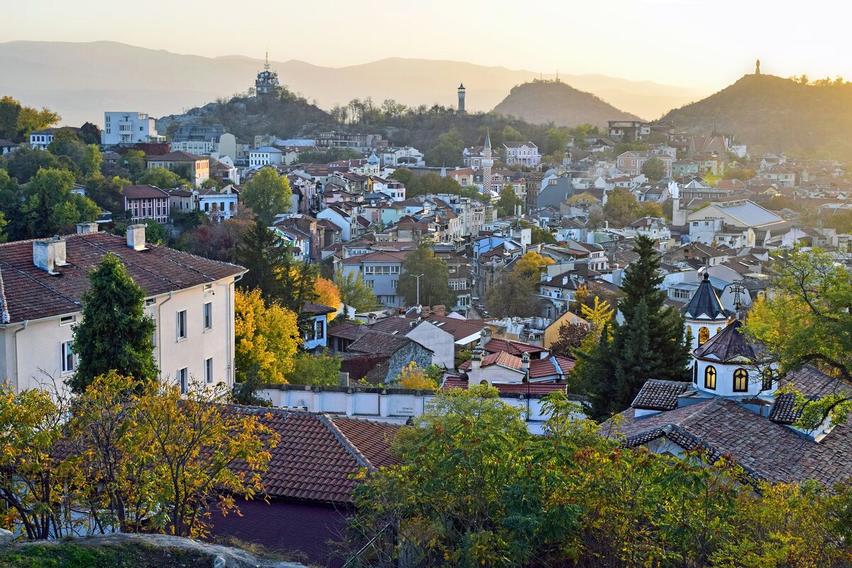 Evening view from Nebet Tepe over the roofs and autumn trees of Old Plovdiv toward the clock tower, Bunardzhik hill with the Alyosha monument and the Rhodope Mountains.