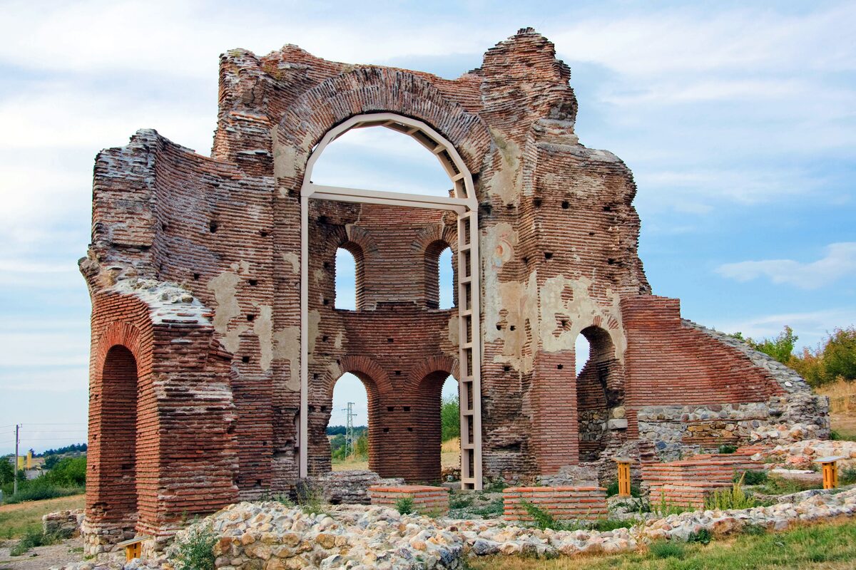 The roofless red-brick ruins of the early Christian Red Church near Perushtitsa, with tall arches held up by a metal support frame.