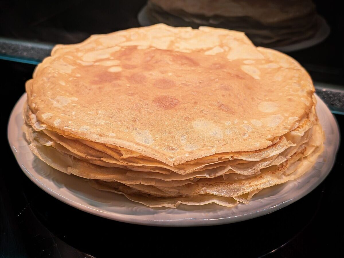 A tall stack of thin golden crêpes on a plate