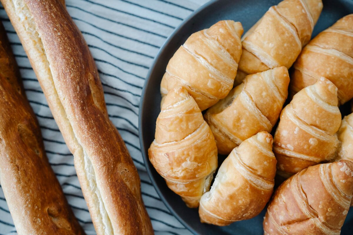 Fresh croissants on a plate next to a baguette on a striped cloth