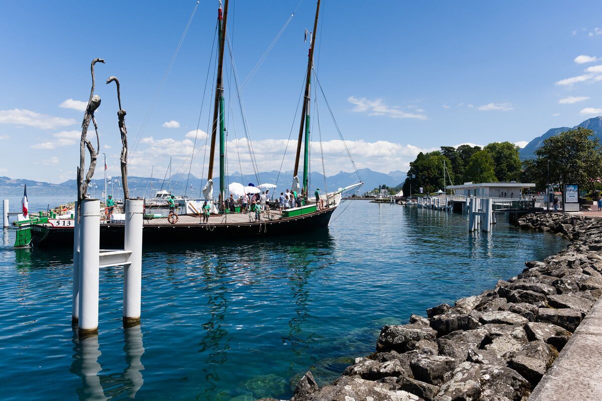 A traditional sailing boat moored in Évian harbor on Lake Geneva, with mountains across the water