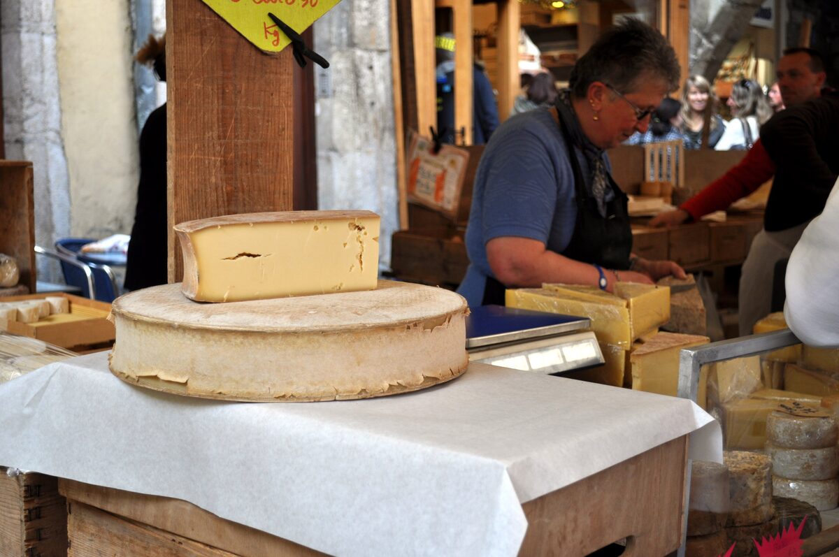 Wheels of Alpine cheese on a market stall with a cheesemonger cutting a slice