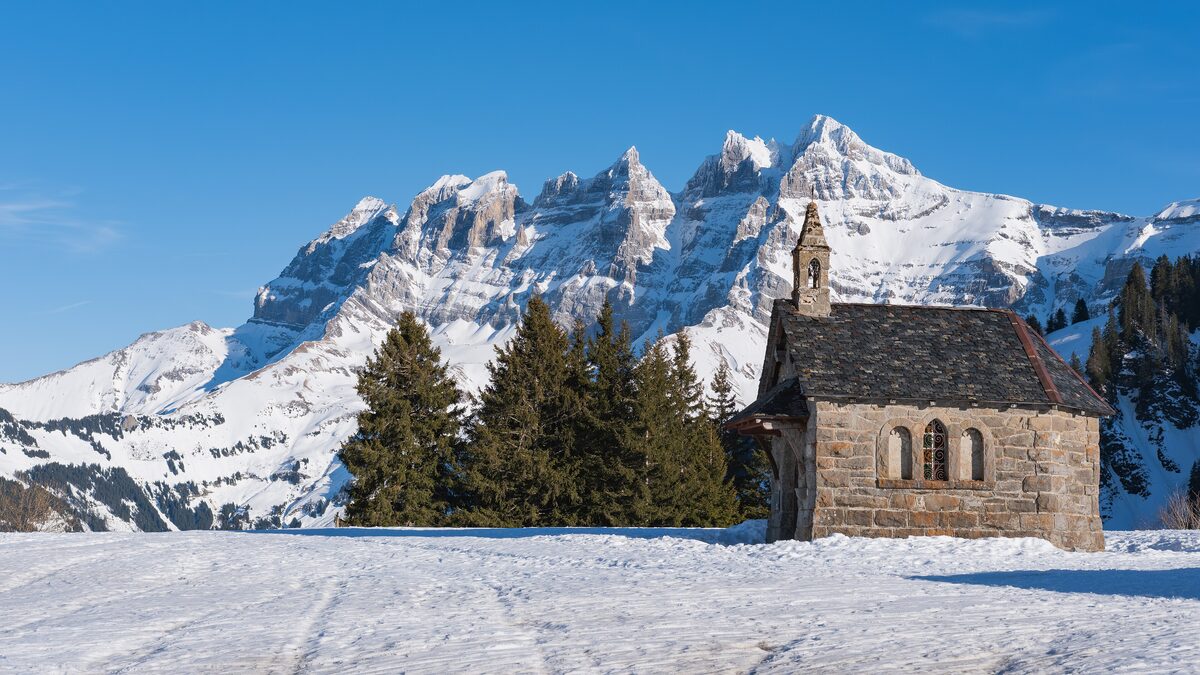 The stone chapel of Les Crosets in snow, with the Dents du Midi peaks behind