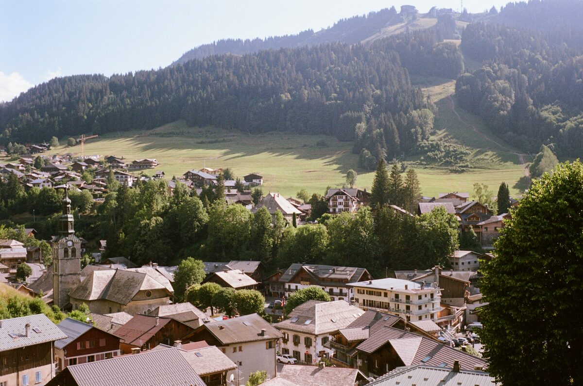 Morzine seen from above on a summer day, with the church tower among the roofs and the green slopes behind