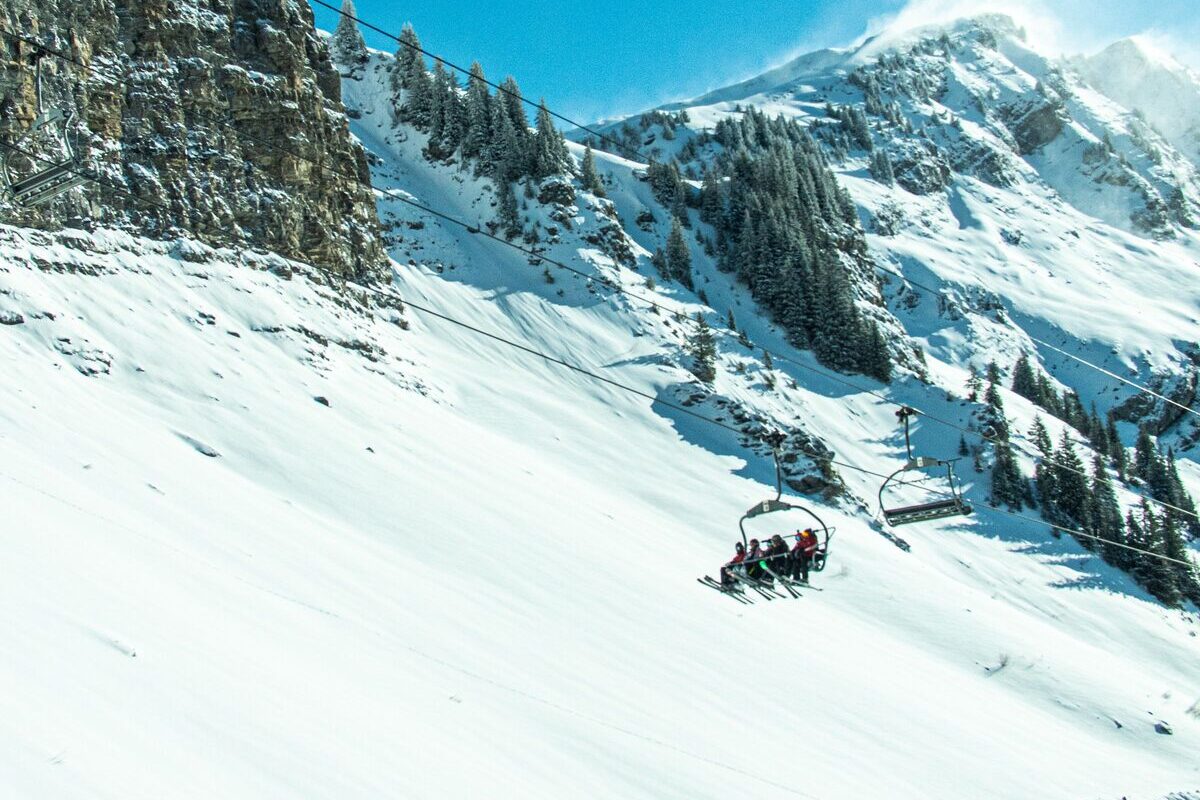 A chairlift carrying skiers over a steep, sunny snow slope under a rock face above Morzine