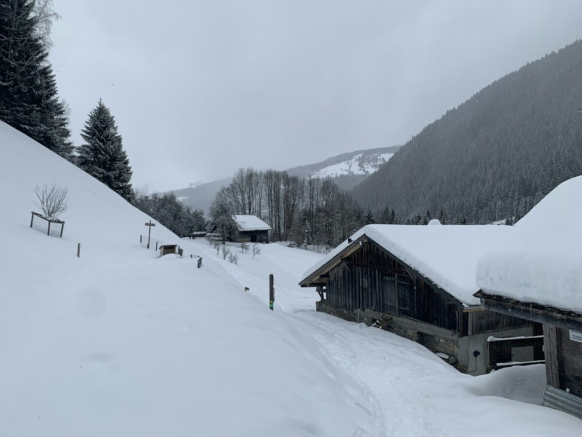 Wooden barns under deep snow beside a snowy track in a Morzine valley