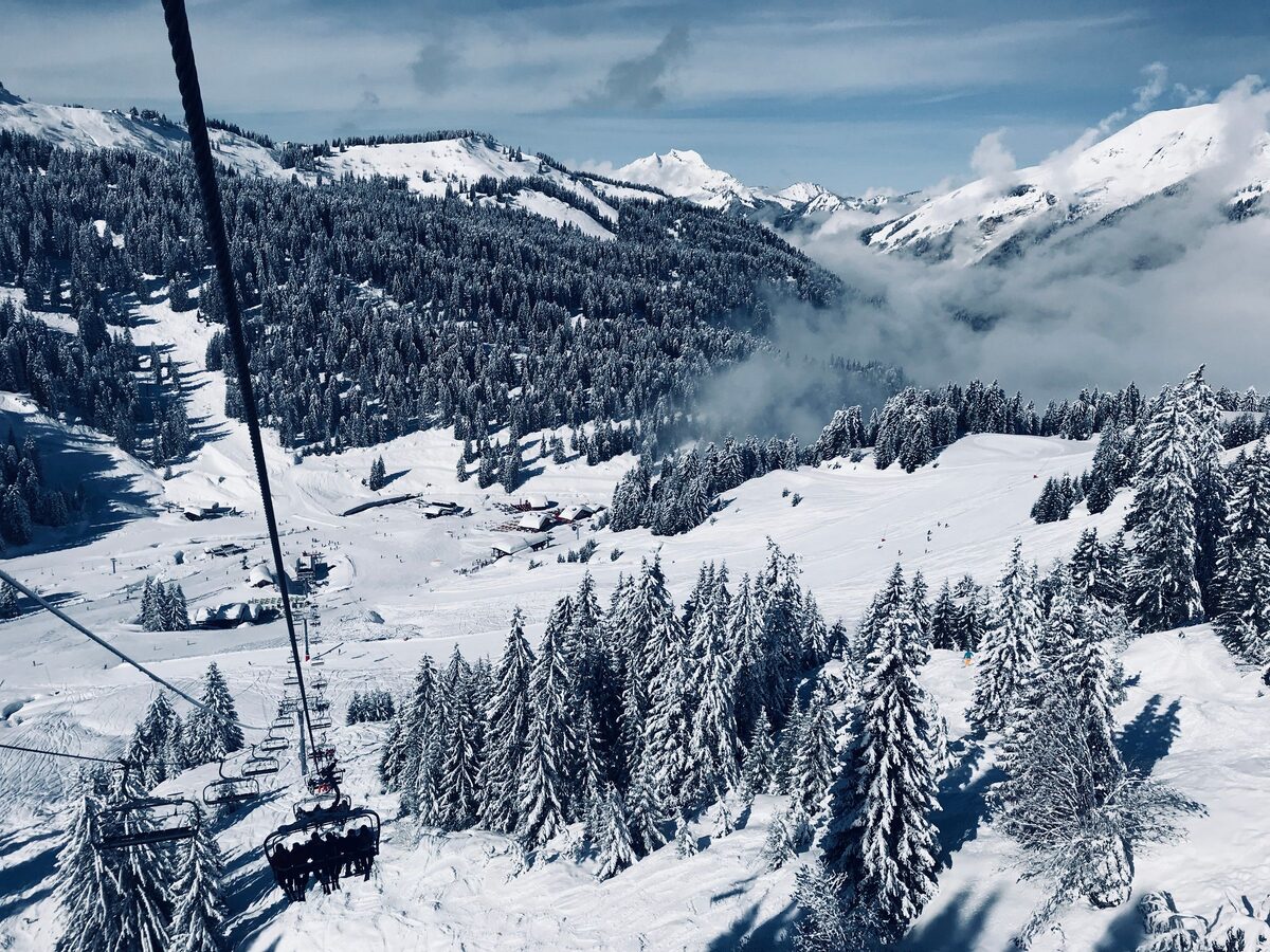 A chairlift running over snowy pines on the slopes above Morzine, with peaks behind