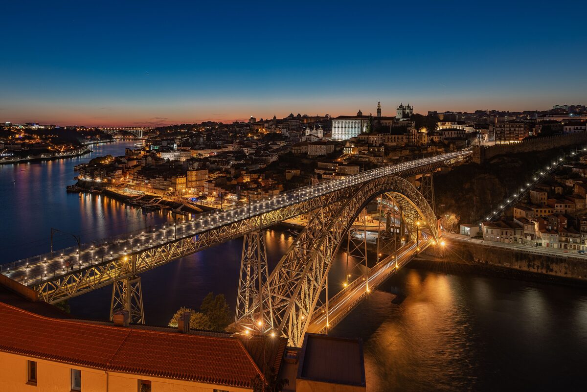 The Dom Luís I Bridge lit up at dusk over the Douro, with the city lights reflected on the water