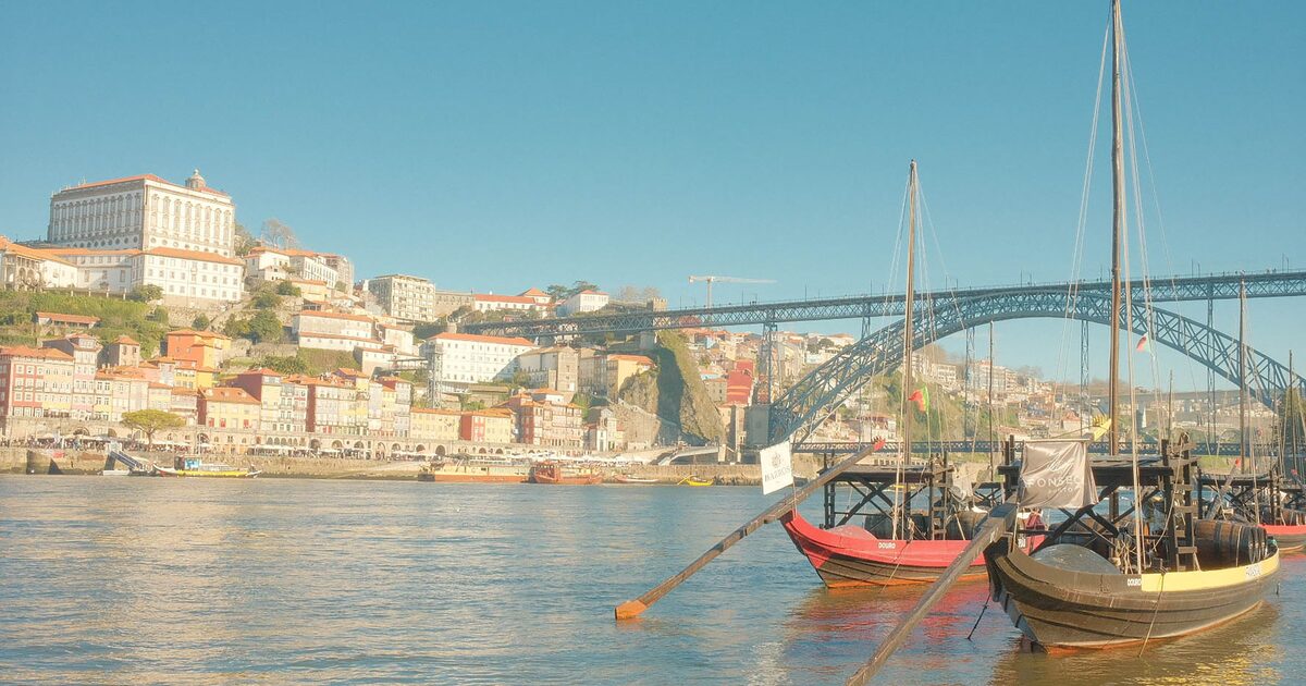 Rabelo boats on the Douro in golden light, with the Ribeira houses, the Bolsa palace on the hill and the Dom Luís I Bridge behind