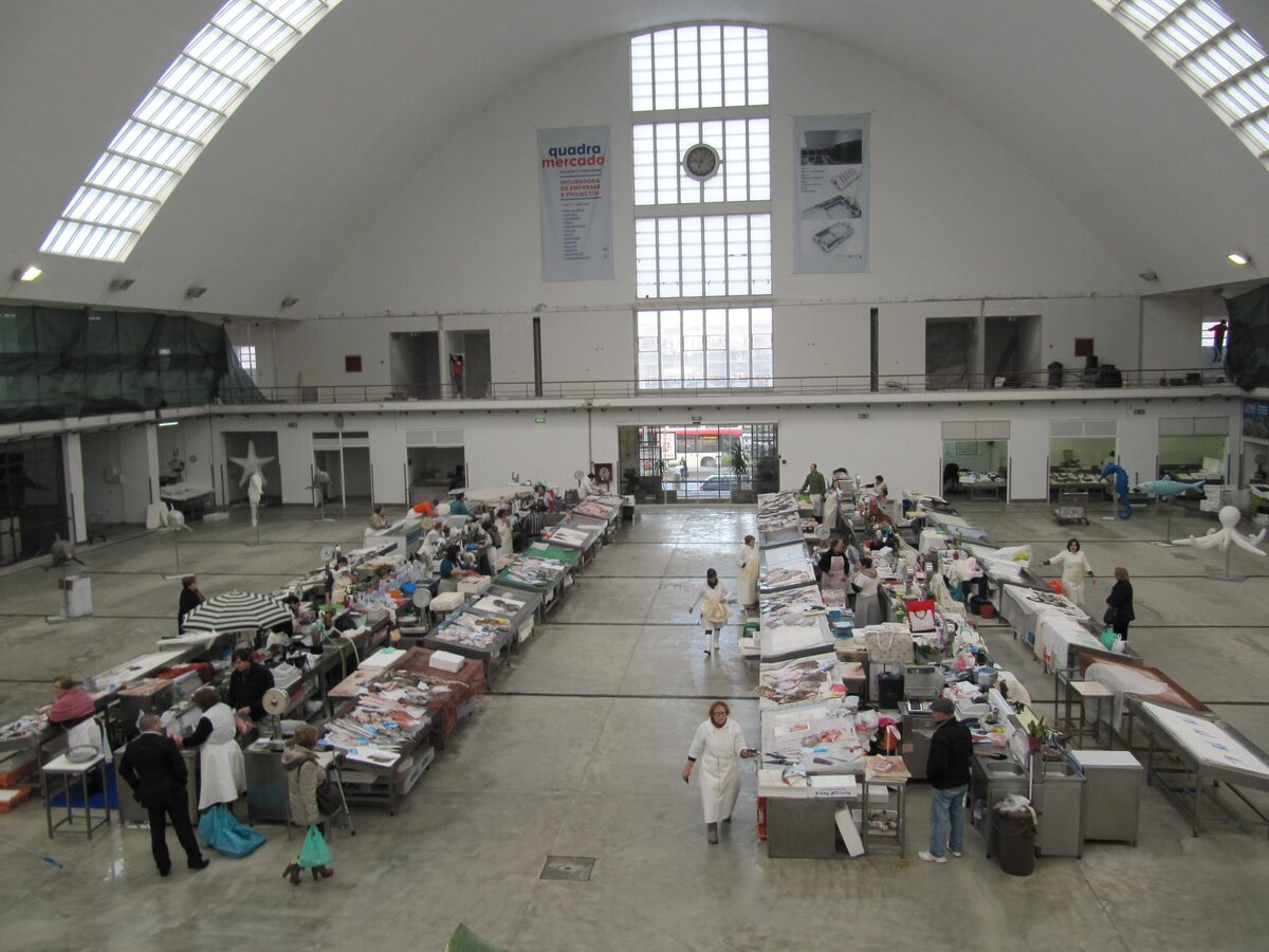 Fish stalls laid out in the vaulted hall of the Matosinhos municipal market, with shoppers and fishmongers between the rows