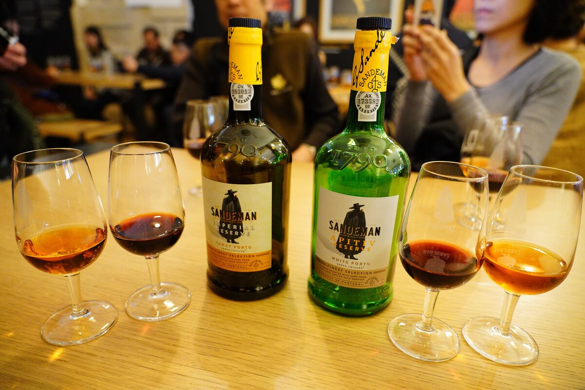 Four tasting glasses of tawny and ruby port on a wooden table beside two Sandeman bottles