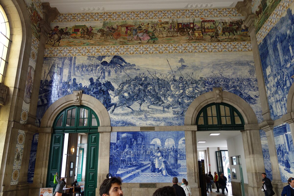 Blue and white azulejo panels covering the walls of the São Bento station hall, with travelers passing the doorways