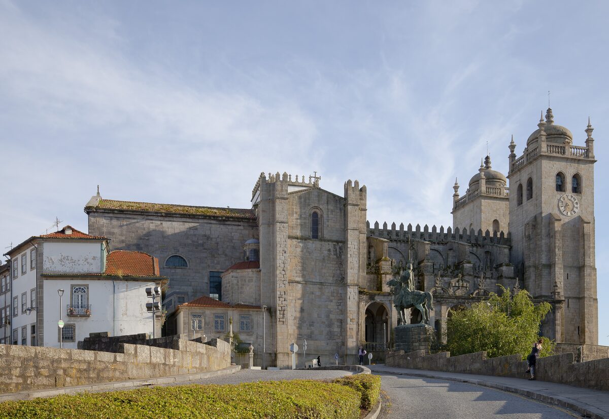The Sé do Porto cathedral seen from the terrace beside it, with its fortified granite walls, crenellations and two square towers under a blue sky