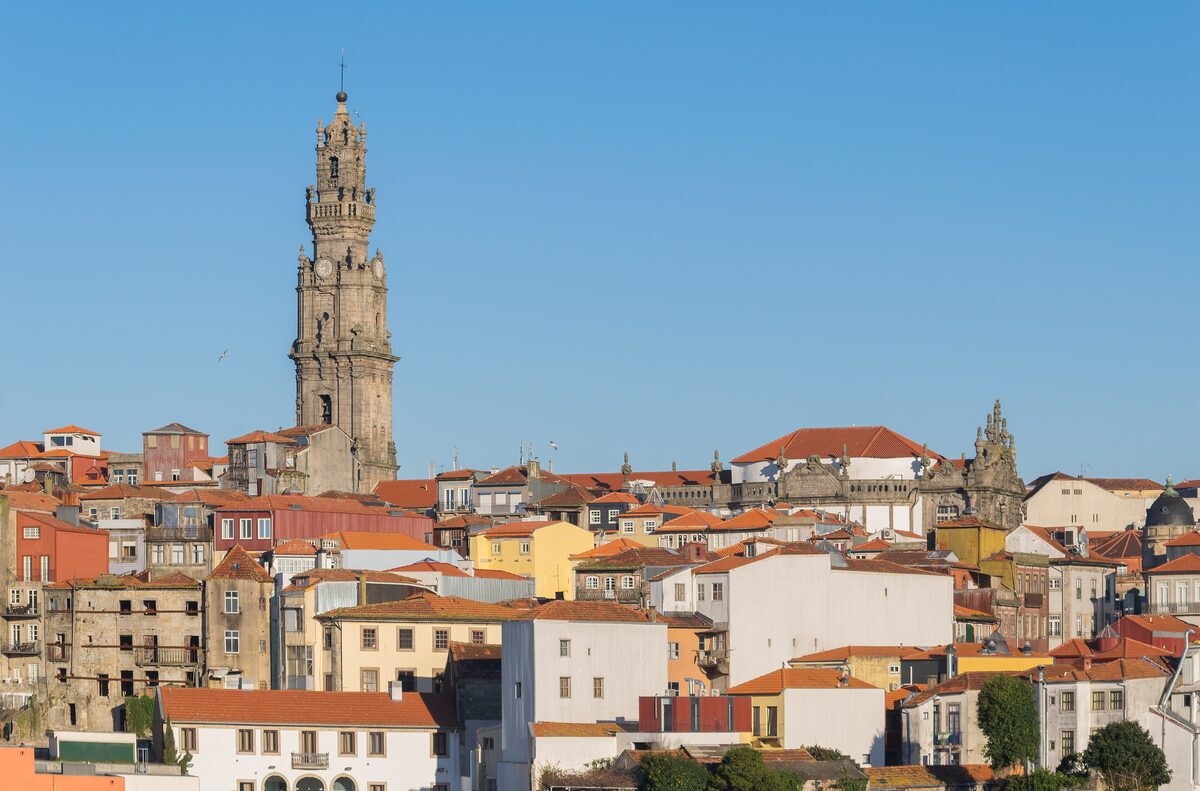 The tall granite Clérigos Tower rising above the red roofs and colorful houses of Porto's old town under a clear blue sky