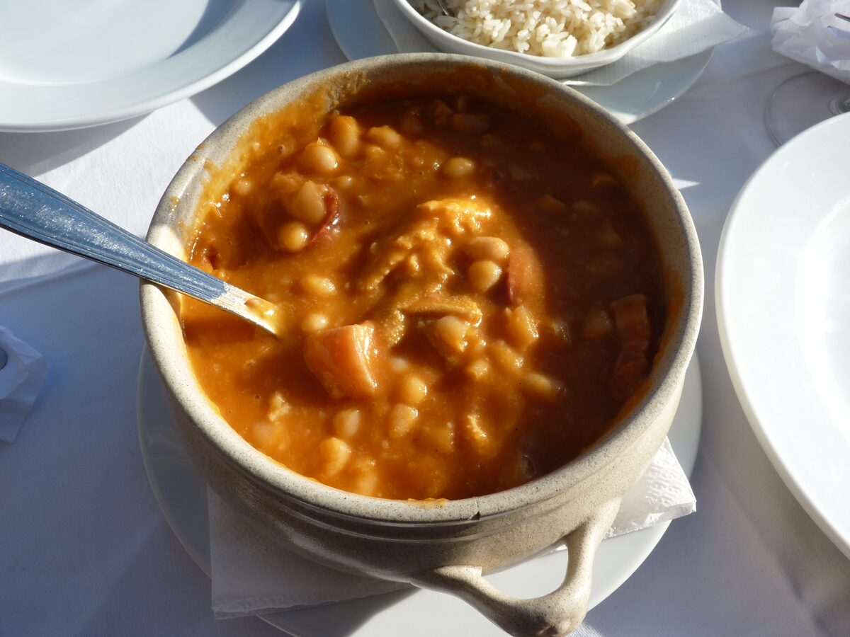 A bowl of bean and meat stew with sausage in an earthenware dish