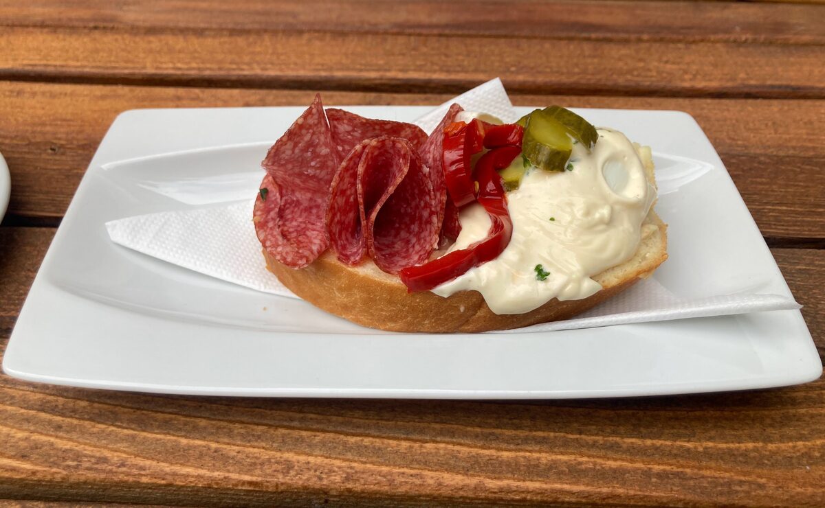 An open-faced chlebicek topped with salami, pickle and roasted pepper on a potato salad base