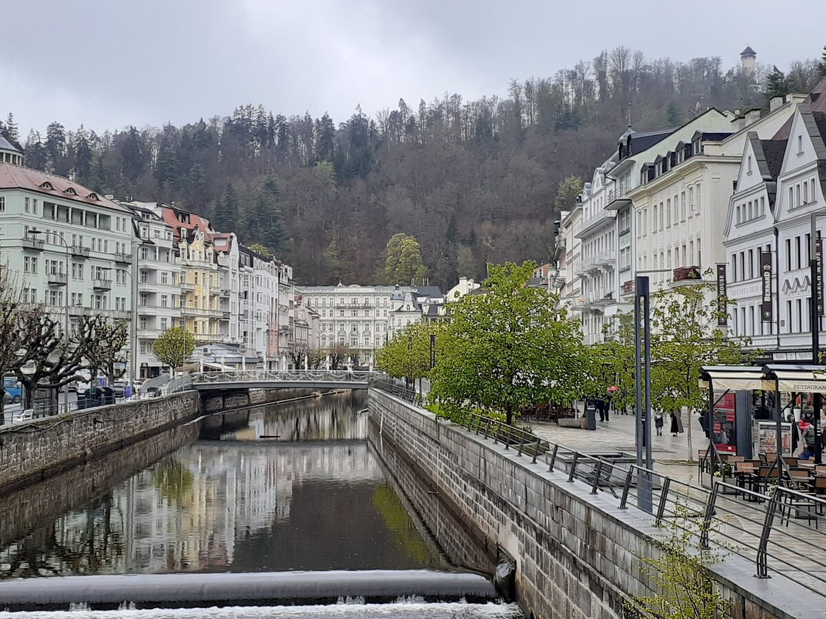 The Teplá river embankment in Karlovy Vary, with hotel facades and wooded hills behind
