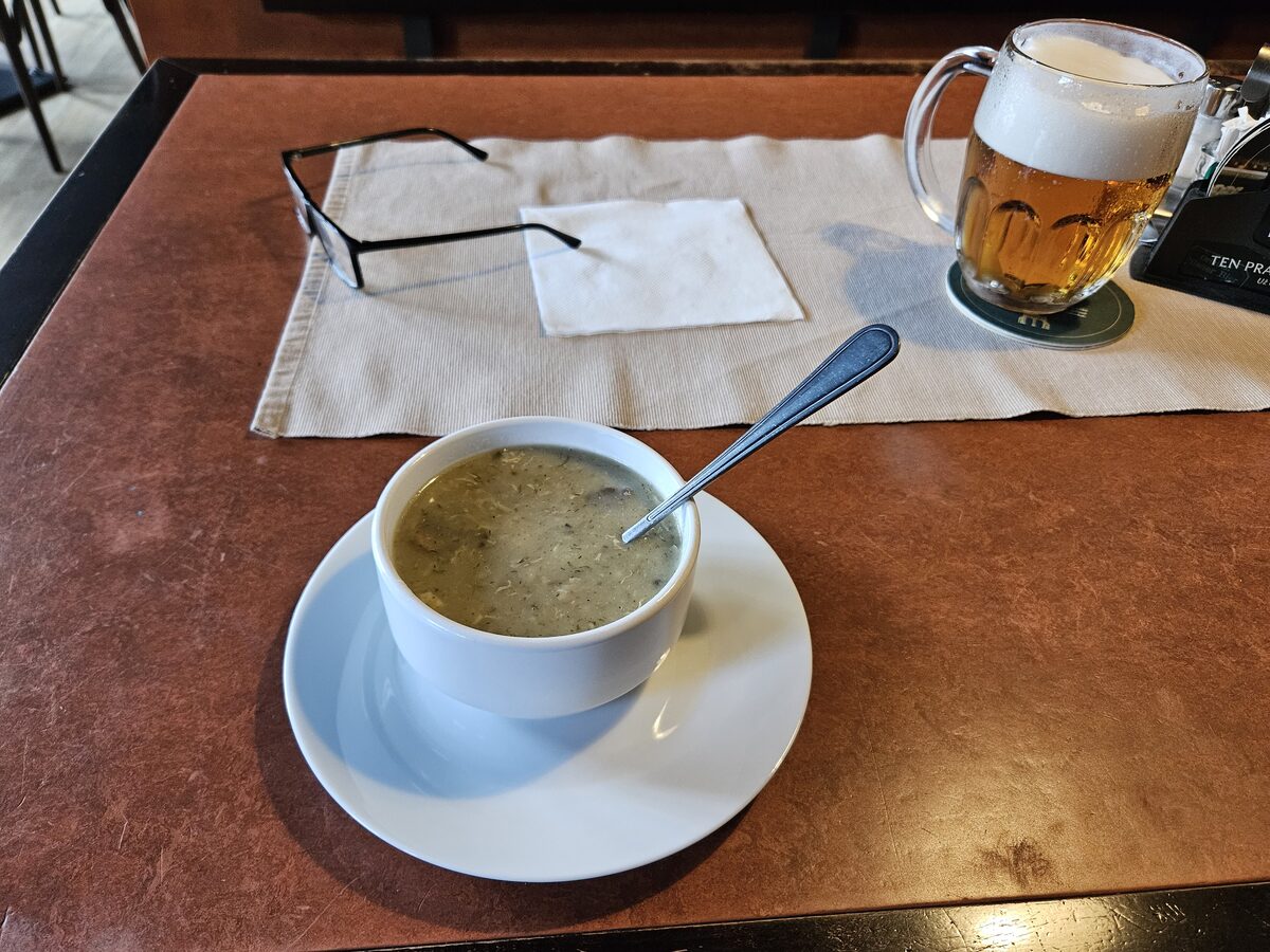 A bowl of soup on a saucer beside a glass of beer on a restaurant table