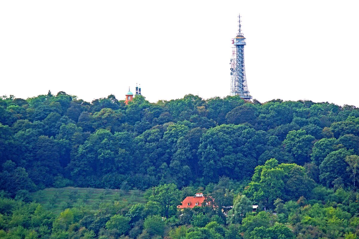 The Petřín Lookout Tower rising above the wooded hill, with a red-roofed house in the trees below