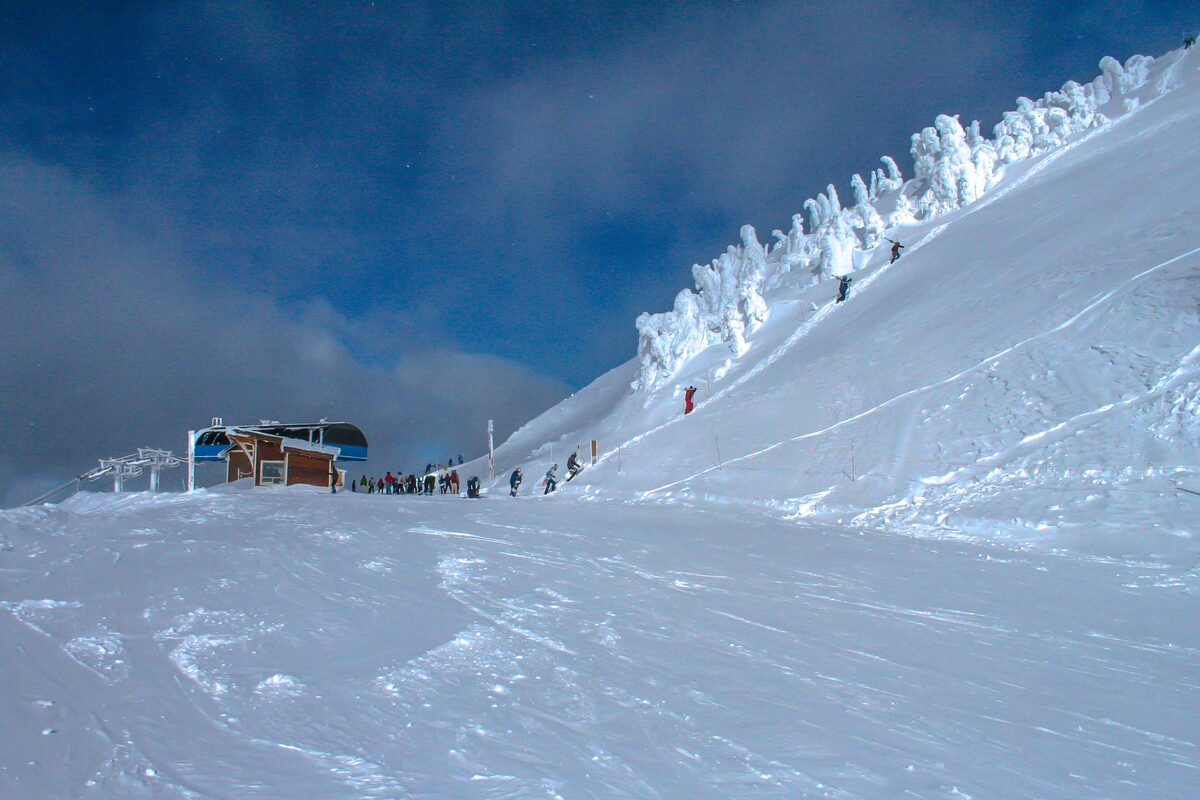 Skiers hike a snowy summit ridge toward the back bowls