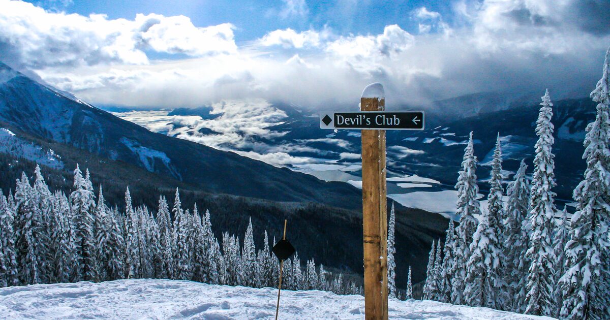 Trail sign and frosted firs above a cloud-filled valley