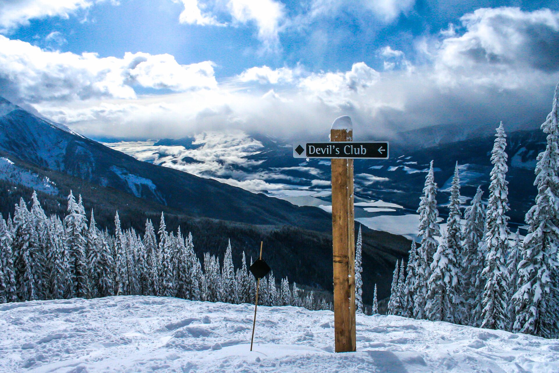 Trail sign and frosted firs above a cloud-filled valley