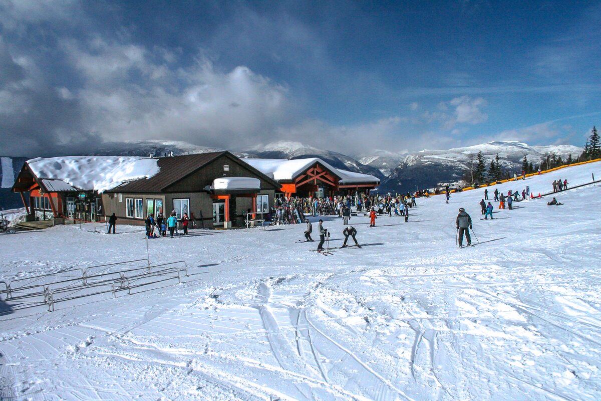 Mid-mountain day lodge with skiers on sunny snow in front