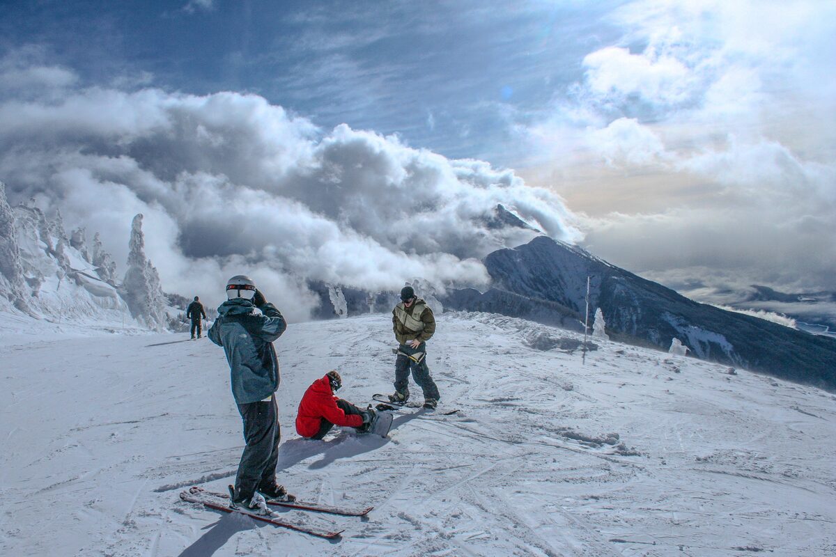 Skiers and snowboarders pause on a summit run beside cloud