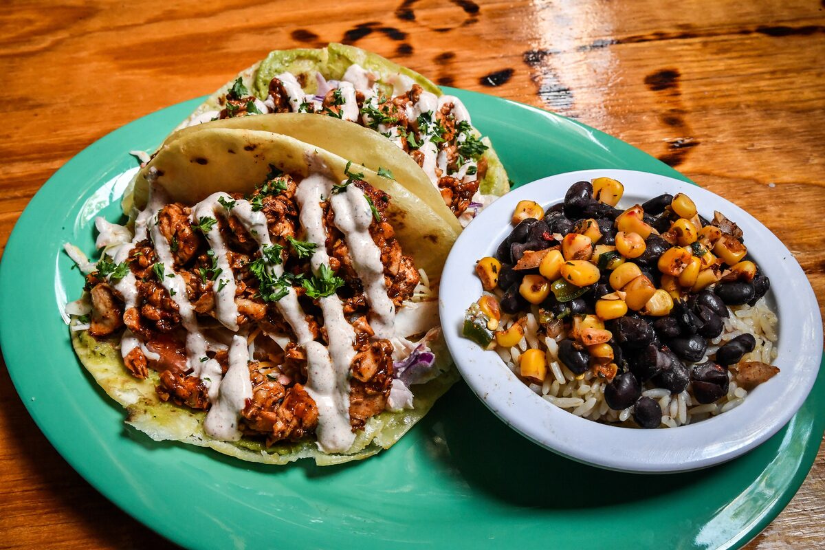 Tacos with creamy drizzle beside a bowl of beans and corn