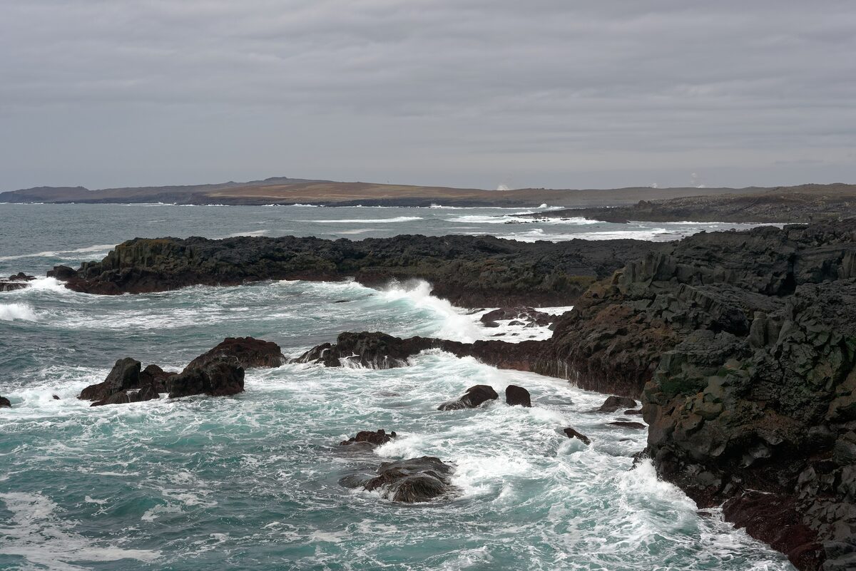 Waves breaking over black lava rock at Brimketill, with a grey sky over the coast