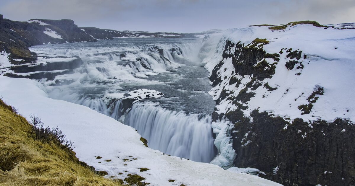 Gullfoss in winter, the river pouring over snow-covered black rock under a pale sky