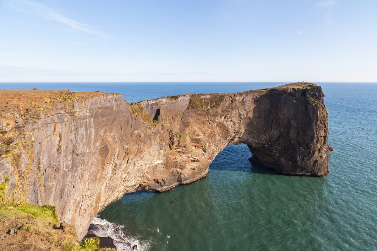 The natural sea arch of Dyrhólaey, a tall brown basalt headland with the ocean flowing through the arch