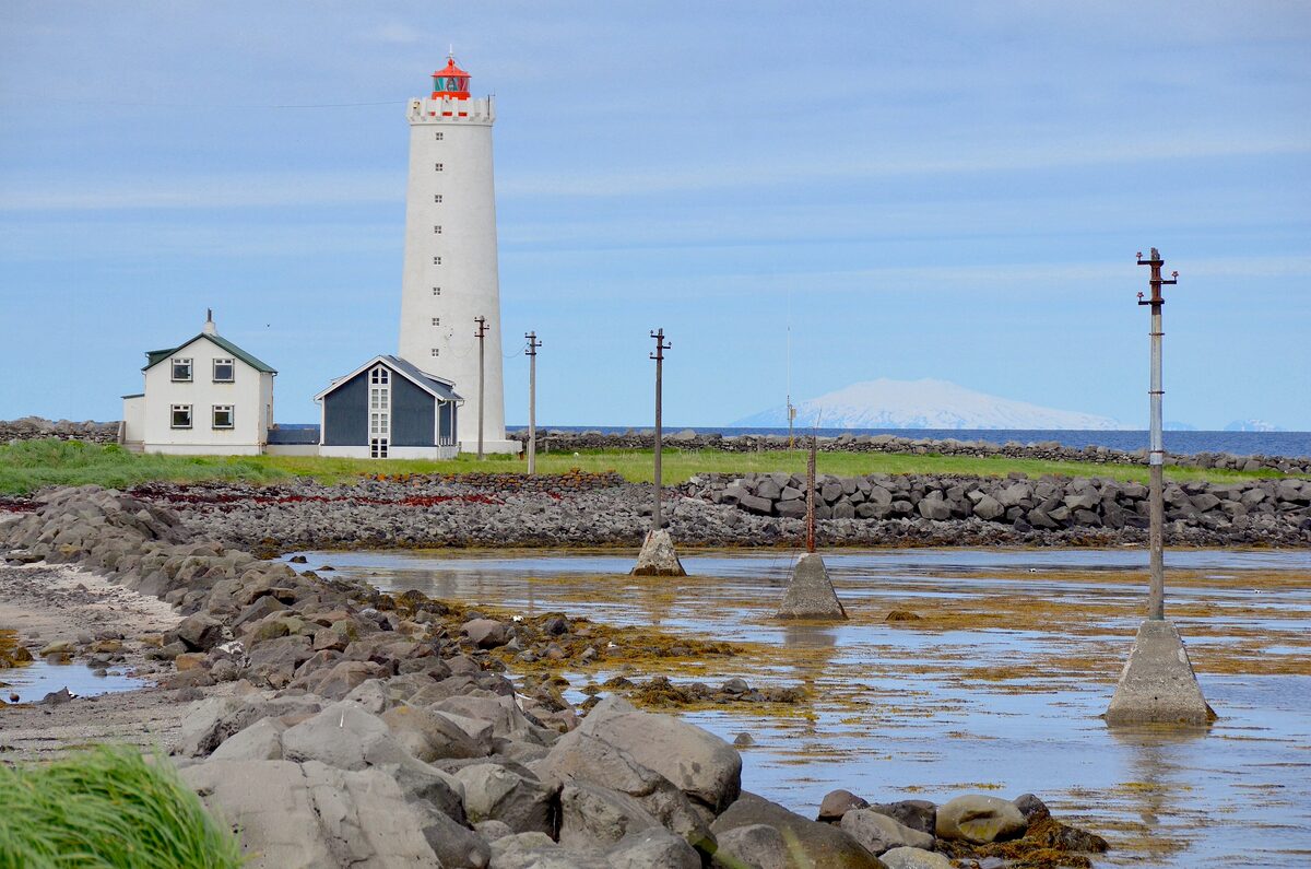 Grótta lighthouse on the rocky shore with a snowy mountain on the horizon