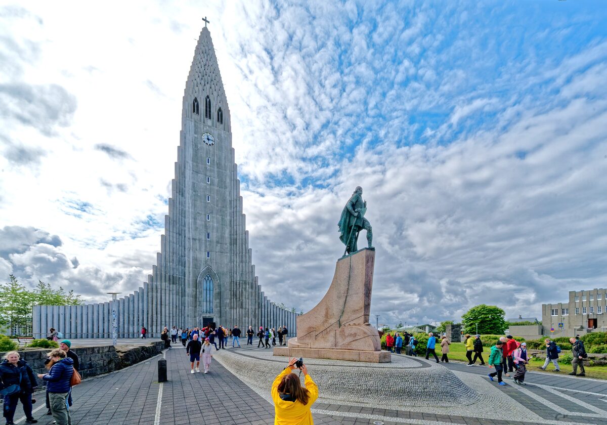 Hallgrímskirkja's tall concrete tower and the statue of Leif Eriksson in front of it, under a blue sky with scattered clouds