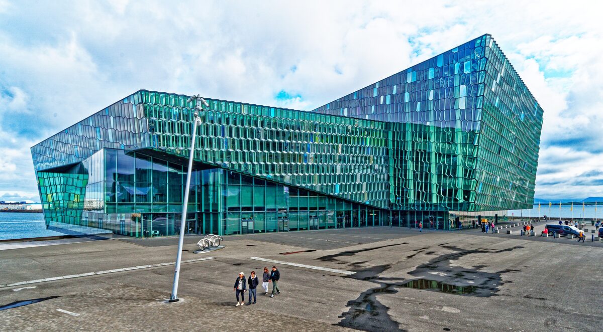 Harpa concert hall's green and blue glass facade in daylight on the harbour edge, under a blue sky with clouds