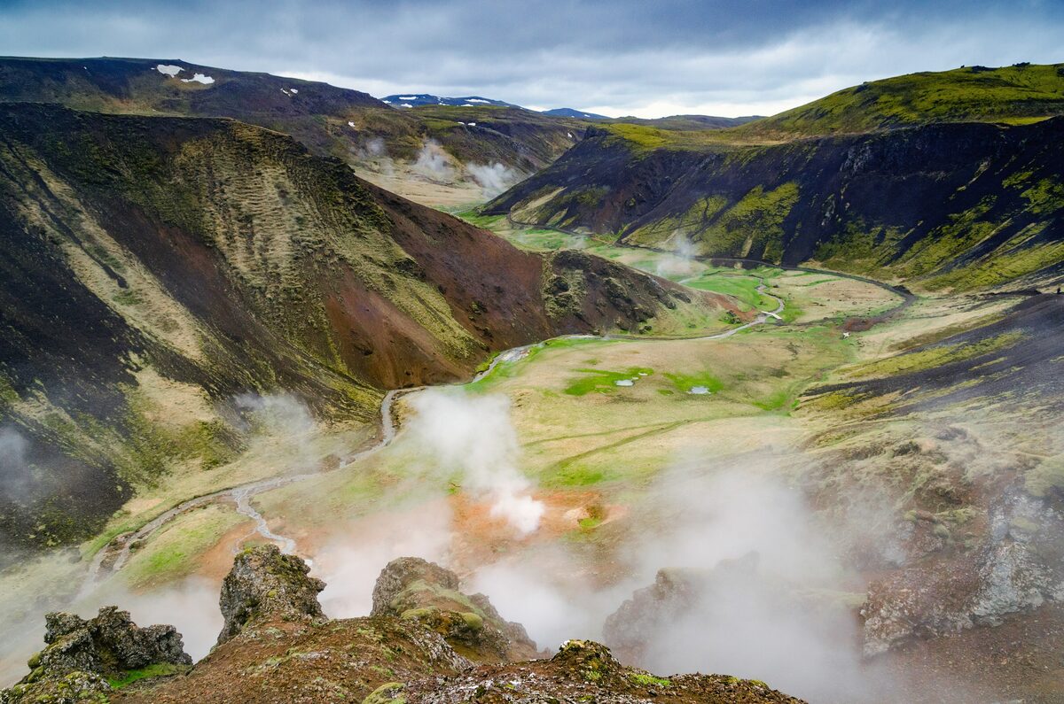 Steam rising from geothermal vents in the green and rust-colored Reykjadalur valley above Hveragerði