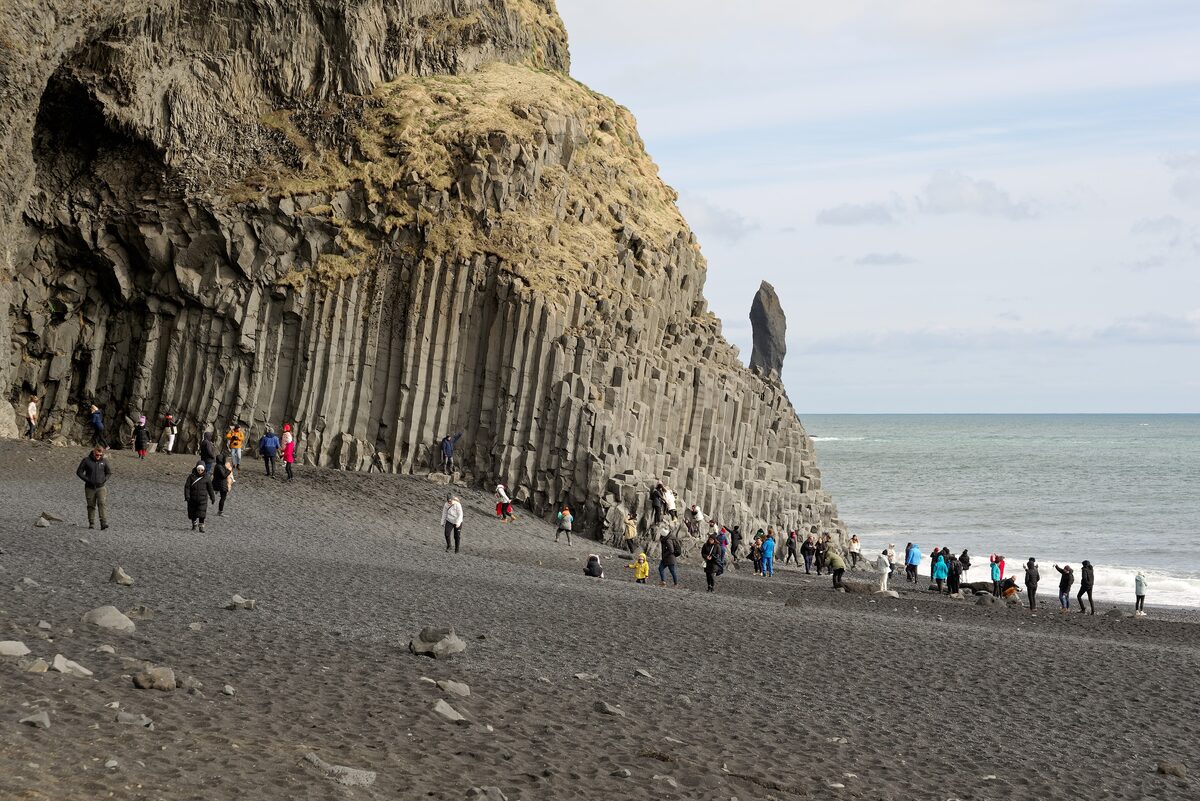 Reynisfjara black sand beach with basalt columns and a sea stack, visitors walking on the sand