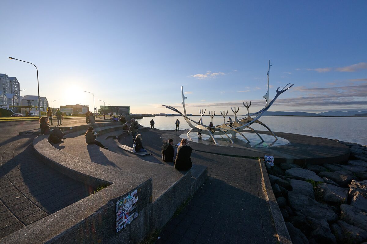The Sun Voyager steel ship sculpture on the waterfront at sunset, with people sitting on the curved wall beside it