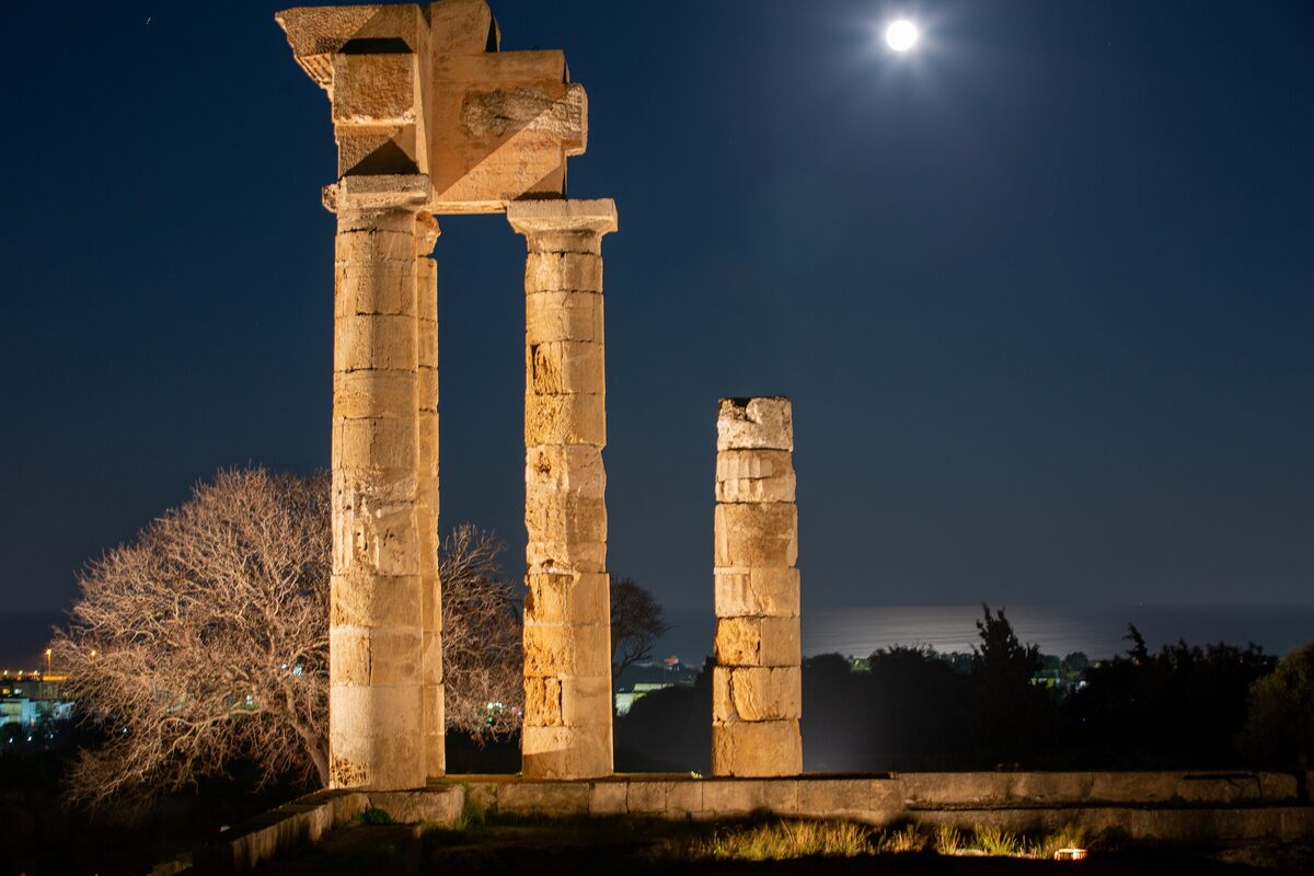 Two restored columns of the Acropolis of Rhodes lit up at night, with a full moon above them