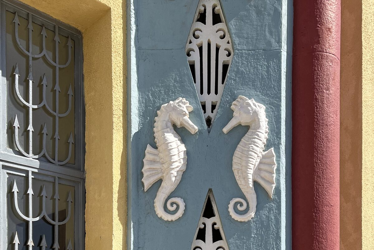 Two white seahorse reliefs on the blue and yellow facade of the Rhodes Aquarium building