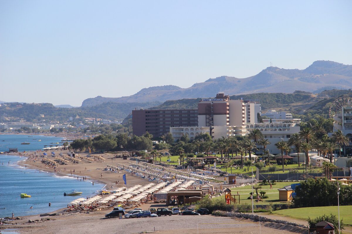 Faliraki beach with rows of sunbeds, palm trees and beachfront hotels below the hills